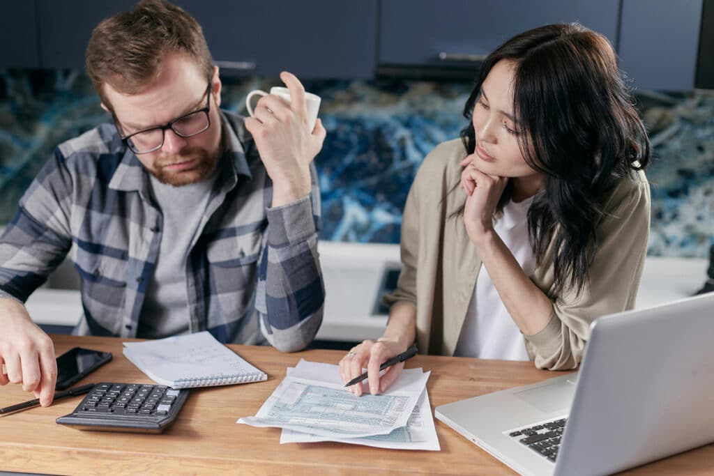 Two people reviewing project costs while using construction project management software at a desk.