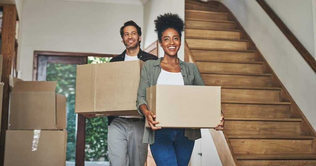 Happy couple, real estate and moving in new home with boxes for renovation, investment or relocation. Interracial man and woman owner carrying box for property rent, mortgage loan or move together.