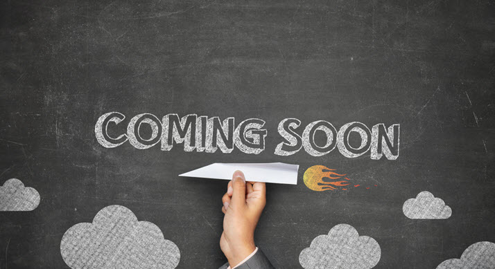 Words "Coming Soon" are written on a chalkboard with a hand holding a paper airplane below.