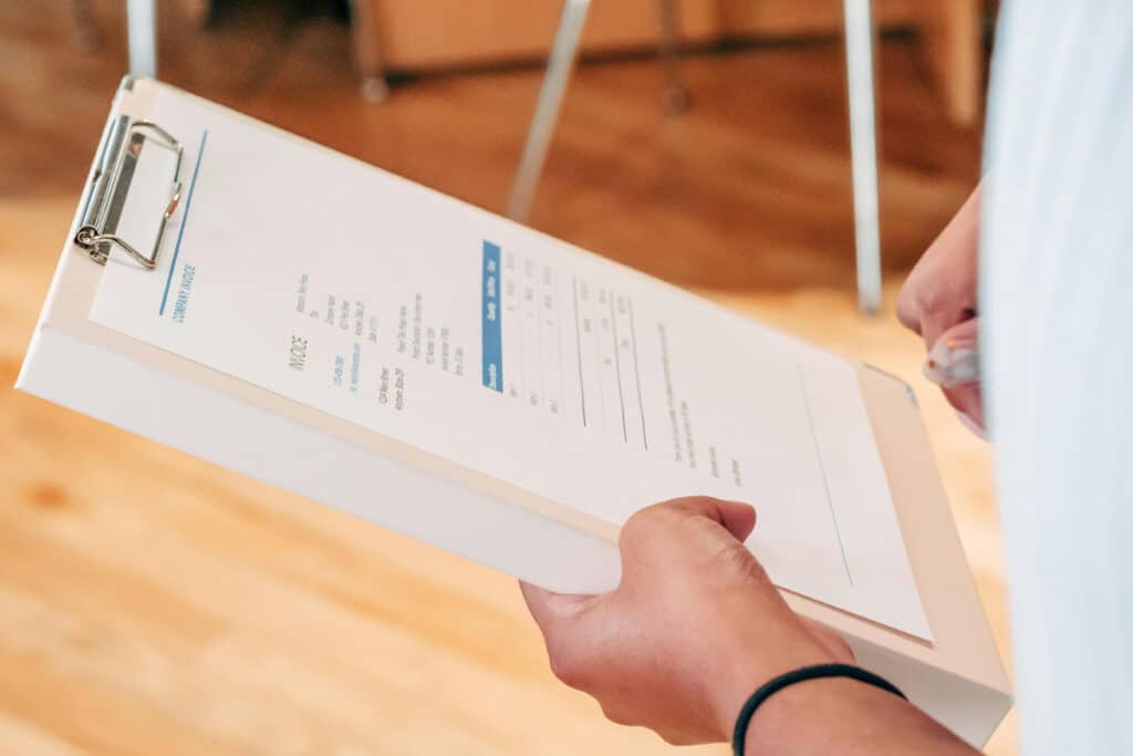 Person holding a clipboard with an invoice while calculating markup and margin for a project.