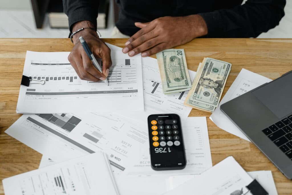 Person reviewing financial documents with cash, calculator, and laptop showing a contractor estimating software.