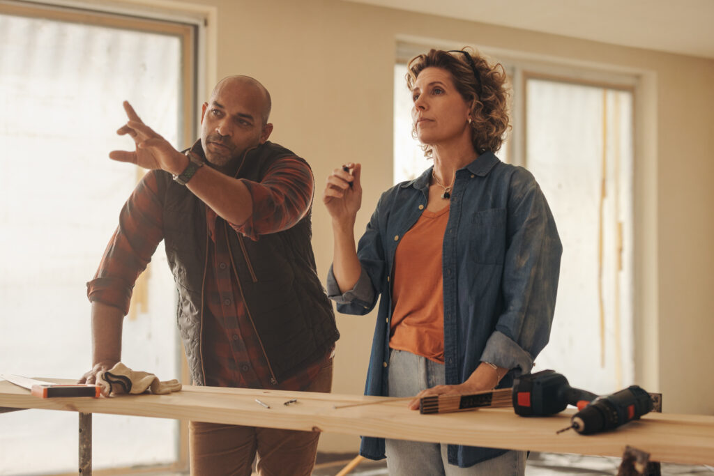 Homeowning couple collaborating on a home renovation project, discussing ideas and planning together. They work diligently indoors, engaging in carpentry and remodeling using wooden planks.